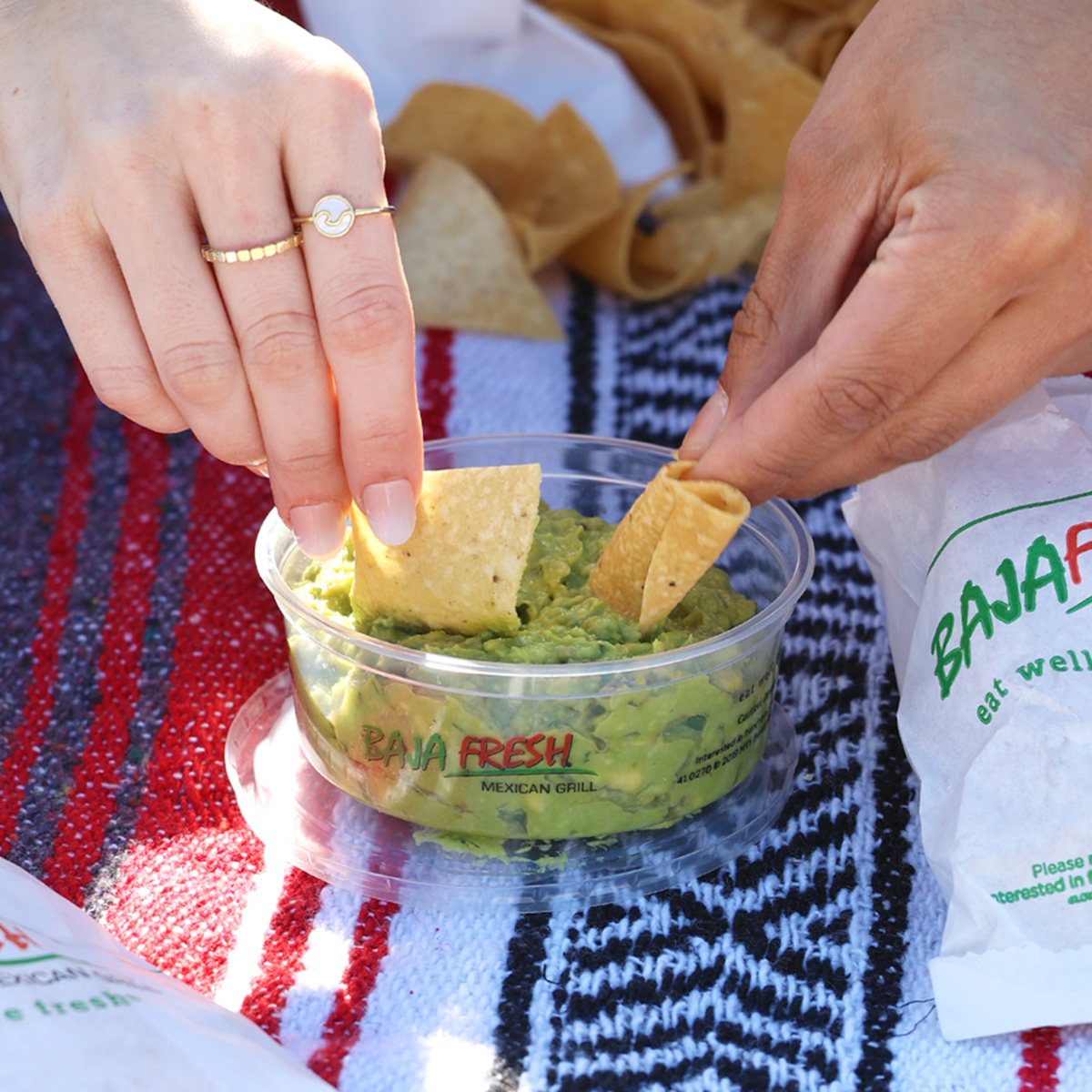Hands with chips dipping in guacamole