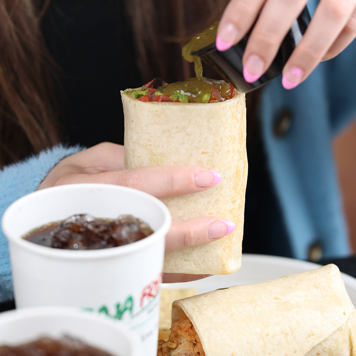 Hands pouring salsa over burrito